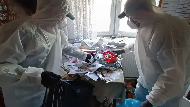 Messie Entrümpelung 1030 Wien Landstraße – Team in Schutzanzügen Messie Entrümpelung 1030 Wien Landstraße: zwei Mitarbeiter in Schutzanzügen und Masken gehen Papiere am Tisch vor dem Fenster durch